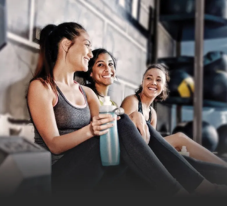 Three smiling members taking a break together on the gym floor at ZUM Fitness