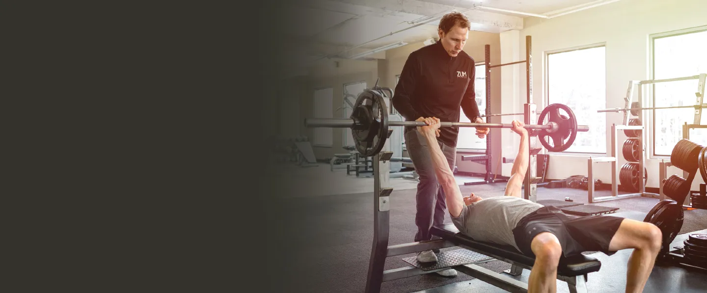 A ZUM trainer spotting a member on the bench press
