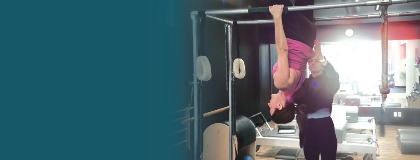 Member inverted on the Pilates Cadillac with a trainer spotting